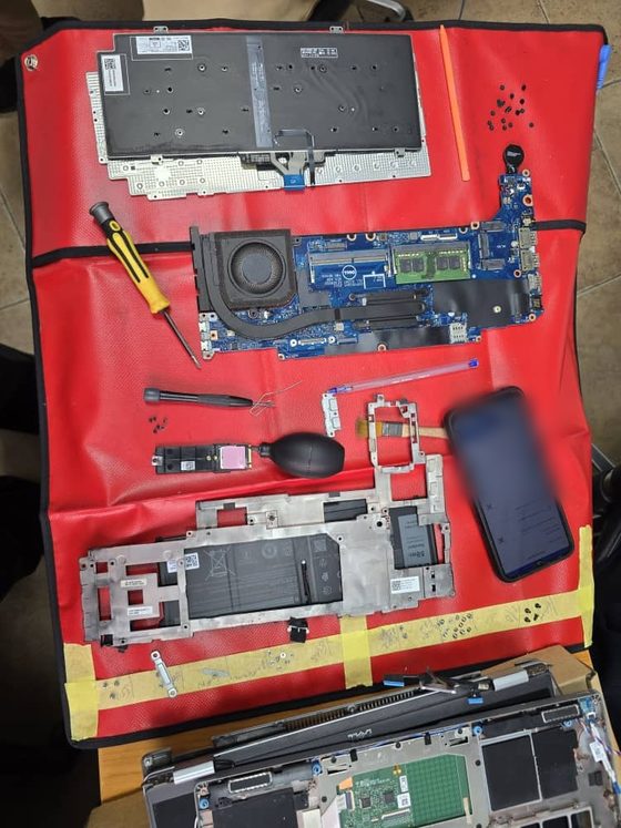 A business notebook stripped to its components on a field ESD mat during an onsite repair: system board with memory fitted, battery, heatsink and fan, storage board, display assembly and chassis.